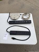 Photo showing three power strips on a white table in outdoor light, different sizes and cord types.