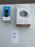 Ring Video Doorbell and August Wi-Fi Smart Lock boxed items on table with auction lot tag
