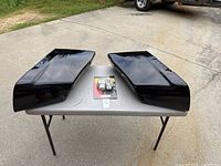 Top view on table of two black plastic motorcycle saddle bag lower portions with packaged switch housings in center