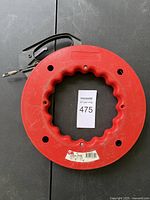 Steel tape measure in red plastic reel casing with metal handle for tape rewinding shown face up on black surface.