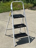 Full view of a white 3-step ladder with black nonslip steps on concrete surface outdoors
