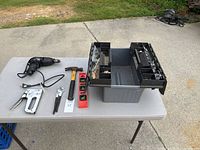 Electric drill, hammer, staple gun, channel locks, level, and tool box with contents on an outdoor table