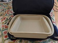 Image showing square and rectangular beige stoneware baking pans placed inside a black carrying case with zipper open.