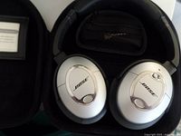 Silver Bose QuietComfort 2 wired noise cancelling headphones inside a black hard carrying case with a mesh pocket inside the lid.