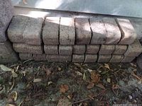 Stack of curved corner interlocking bricks arranged outdoors on dirt ground showing three rows of bricks.