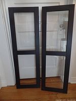 Two Ikea Havsta cabinet doors with glass panes and dark wood frames shown standing vertically side by side.