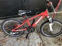 Side profile of red Giant kids bike showing frame, saddle, wheels, pedals, and handlebar.