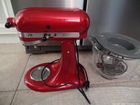 Front view of cherry red stand mixer body with power cord and glass bowl beside it