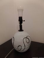 Full view of the ceramic lamp showing the white globular base with black swirl design, fitted with a light bulb and socket.