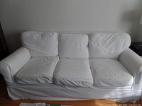 Front view of large white couch with three seat cushions and white slipcover, showing visible use and slight wrinkling.