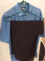 Blue Nike short sleeve golf shirt on hanger with black golf pants draped over it