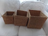 Three square sea grass baskets nested inside each other on a white fabric couch showcasing size differences and texture.