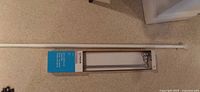 White shower tension rod next to Moen towel bar packaging on carpeted floor