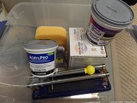 Photo showing manual tile cutter, yellow sponge, two containers (one Acrylpro adhesive, one grout), and a box of powdered grout.
