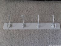 White coat hooks on a 24-inch white wooden base, showing all four double hooks mounted and visible.