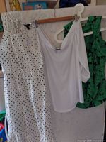 Three women's tops and dress hanging on white hangers. Left: white polka dot midi dress. Middle: white off-the-shoulder blouse. Right: green and navy sleeveless blouse.