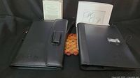 Photo showing black faux leather notebook and matching photo frame, both embossed with Avon logo, placed side by side