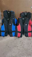 Four Fluid life jackets arranged in two rows against beige background, two red/black and two blue/black, sizes small and large.