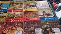 Photo of 14 Family Circle cookbooks laid out with varied colorful covers showing food dishes including pies, cakes, meats