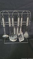 9-piece stainless steel kitchen utensils on metal stand, including ladle, slotted spoon, spatulas, masher, and other tools.