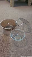 Three Pyrex glass bowls in different sizes and colors placed on carpet floor