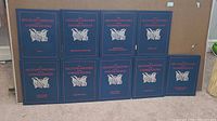 Overview of all nine volumes of the set, showing the dark blue hardcover binding with the title and decorative emblem in red and white.