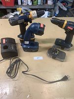 Photo of two Ryobi cordless drills, one cordless flashlight, and a battery charger arranged on a table.