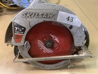 Close view of the corded handheld circular saw with visible Skilsaw branding and red circular saw blade.
