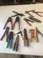 Overview of 14 miscellaneous electrical hand tools including wire cutters, crimpers, wire strippers, and pliers mostly with red handles.