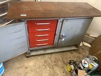 Front view of the metal tool cabinet showing red drawers open within the cabinet and gray doors ajar, on wheels.
