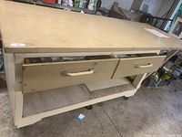 Photo of the front of the large wooden work table showing two drawers with metal handles and lower shelf, on casters.