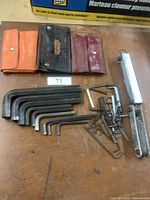 Photo showing all Allen keys of various sizes, three different carry pouches, metal spring clamp, and a boxed metal measuring tool on wooden surface.