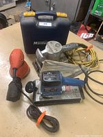 Four electric sanders arranged on a table with a Mastercraft carrying case behind them, showing the individual sanders and cords.