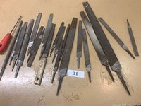 Top side view of metal files and rasps arranged on a workbench showcasing different shapes and sizes, including those with handles.
