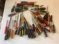 Top view of over 30 assorted screwdrivers laid out on a white surface, showing variety of handle colors and shaft lengths.
