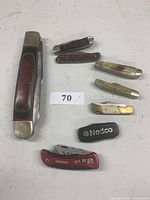 Overview photo showing all 8 folding pocket and utility knives, one large wooden handle knife and seven smaller knives with various handle materials.