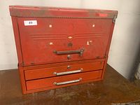 Front view of vintage red metal tool chest showing three front drawers and latch mechanism on the top section with some worn paint spots.
