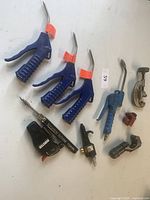 Four blue pneumatic air blow guns with curved metal nozzles, one with adjustment lever, one metal pipe cutter, two copper tubing cutters, and two butane torches.