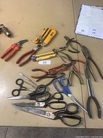 Wide layout showing all cutting tools including various scissors, Olfa cutters, and pliers on a table.