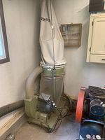 Full view of green shop dust collector with motor, cloth filter bag on top and clear plastic collection bag below, connected hose