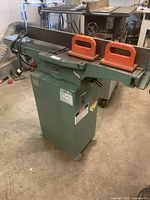 Full view of green pedestal-mounted F.K. Machinery combination jointer/planer with long infeed and outfeed tables and two orange push blocks