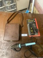 Photo shows the vintage Simpson electrical meter inside brown leather carrying case, black and light blue soldering iron with coiled metal stand, and boxed Amprobe Breakr Tracr device on table.