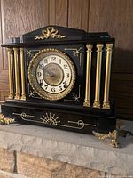 Front and side view of vintage black and gold mantle clock showing decorative columns and clock face.