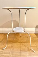 Full view of metal occasional table showing round top, three legs, lower shelf