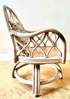 Side view of off-white rattan swivel armchair showing lattice arm and back, floral pillow, swivel base