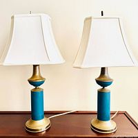 Both matching brass and teal table lamps with shades on wooden surface