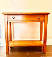 Front view showing top, drawer with knobs, lower shelf and legs