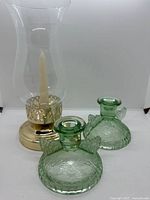 All three candle holders: two green pressed glass and one brass hurricane style