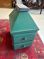 front and side view of green wooden shoe shine cabinet showing two drawers and pyramidal top