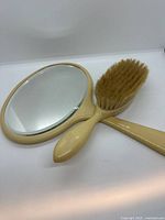Front view of mirror and hairbrush showing cream plastic and bristles